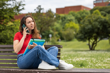 Obraz premium young student woman resting in the park near the university with her notes and her mobile phone