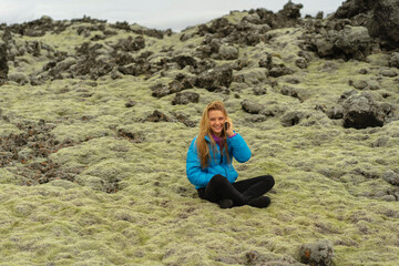 Woman traveler sits on moss in Iceland and calls on the phone.