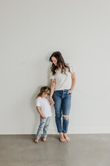Mother and daughter stand together while holding hands indoors