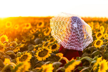 Woman with lace parasol surrounded by sunflowers at sunset.