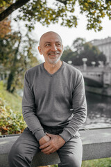 Fototapeta premium Elderly man sitting on a bench near a river, smiling, enjoying the day