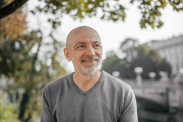 Elderly man smiling warmly while sitting in a park, trees and river