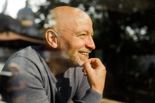 Elderly man with a thoughtful expression through a glass window - Powered by Adobe