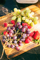 Fresh grapes and berries on a wooden board at an outdoor gathering