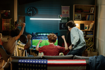 Rear view of ethnically diverse male friends spending evening in living room watching soccer match on TV, copy space