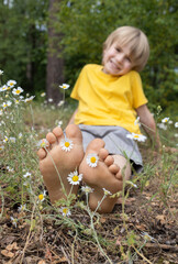 happy barefoot child resting while sitting among a chamomile meadow in the forest. positive atmosphere, joyful childhood. Hello summer. relaxing energy of nature. Earth Day. selective focus