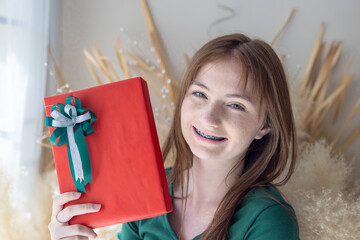 Young woman unwraps Christmas gift in festive home with holiday decor, capturing holiday joy.