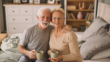 Happy elderly couple enjoying coffee or tea in bed 