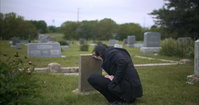 Man mourning over death of loved one at grave tombstone in cemetery.
