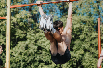 Athlete executing leg raises on a horizontal bar in an outdoor park. Fitness training in sunny...