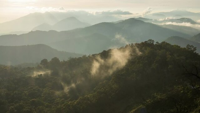 Mist swirling back light from soft morning sun on volcano mountainous layered hillside.  Kawah Putih sunrise, Indonesia, 
dynamic light, time lapse.