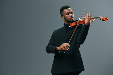 African American man in black suit playing violin with passion and skill on gray background