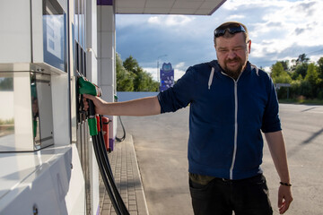 A man wearing a blue jacket is filling up a car with gas at a gas station.