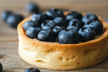 Homemade mini tart with blueberries and whipped cream on a wooden background, close up.