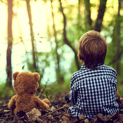 Young boy, teddy bear and back for outdoor adventure in forest for exploration with companion in...