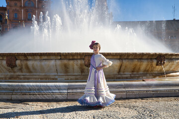 Girl dancing flamenco, posing looking at camera, in typical flamenco costume next to spectacular fountain in a beautiful square in Seville. Dance concept, flamenco, typical Spanish, Seville, Spain.
