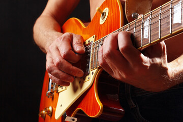 Hands of rock guitarist playing the orange guitar on dark stage.