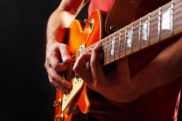 Rock guitarist in red plays the orange electric guitar on dark stage.