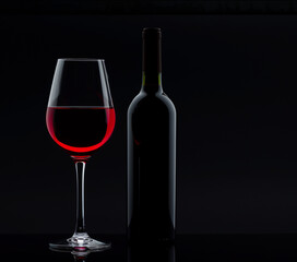 Glass with red wine and bottle next to it on a black background