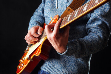 Artist in blue sweater plays the orange electric guitar on dark stage.