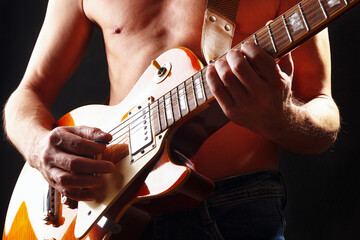Musician plays the orange sunburst electric guitar on dark stage.