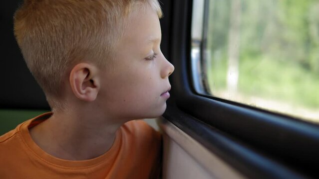 Close-up of a little boy riding a train and looking out the window. A child is a passenger, a boy travels by train in the summer.
