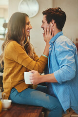 Couple, love and happy in home kitchen, trust and hands on face with people together for relationship bonding. Beverage, commitment and caring partner or smile, apartment and sitting on dining table