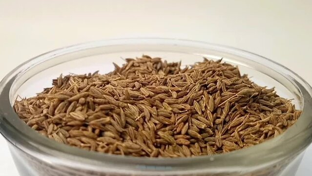 Cumin seeds drops in a glass bowl on white background, a glass bowl full of cumin seeds in the center, rotating, micro shot, herbs and spices.