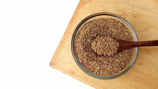 Taking Cumin seeds from the glass bowl with a wooden spoon, top view, herbs and spices