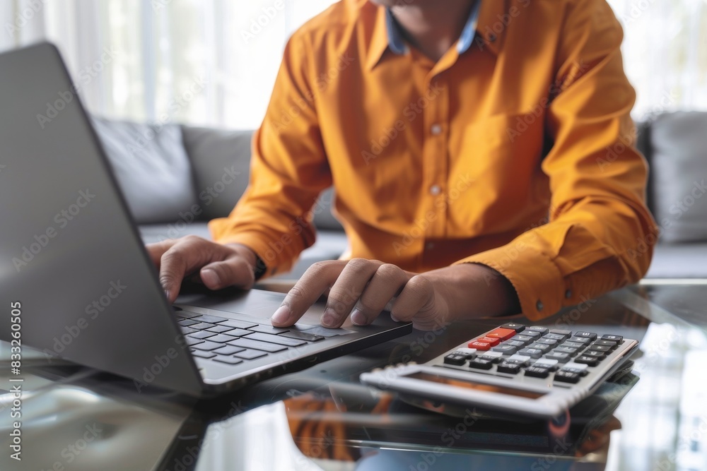 Wall mural close-up photo of a person working on a laptop with a calculator nearby, highlighting a business or 