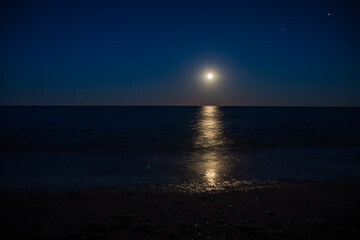 During the night, a bright full moon illuminates the ocean under the sky
