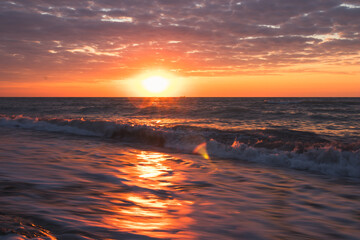 The sun is setting over the ocean, waves crashing on the beach