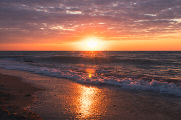 The sun is setting over the ocean, waves crashing on the beach