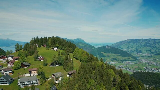 Flying over mountain village with houses on green hill in Switzerland Alps,Stoos