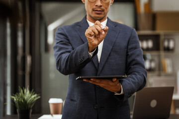 Middle-aged Asian businessman in formal suit working diligently at his desk. seasoned business and investment consultant, specializing in strategic portfolio management and financial analysis.