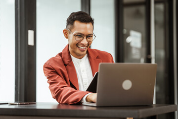 Fototapeta premium Middle-aged Asian businessman in formal suit working diligently at his desk. seasoned business and investment consultant, specializing in strategic portfolio management and financial analysis.