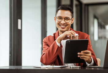 Middle-aged Asian businessman in formal suit working diligently at his desk. seasoned business and investment consultant, specializing in strategic portfolio management and financial analysis.