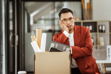 A middle-aged Asian businessman in a formal suit is working at his desk, preparing to resign after...