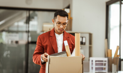 A middle-aged Asian businessman in a formal suit is working at his desk, preparing to resign after...