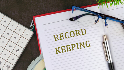 Record keeping text concept on the open page of the business notebook next to the eyeglasses and...