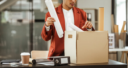A middle-aged Asian businessman in a formal suit is working at his desk, preparing to resign after...