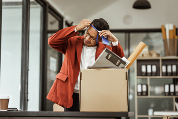 A middle-aged Asian businessman in a formal suit is working at his desk, preparing to resign after...