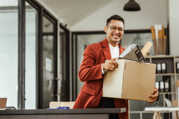 A middle-aged Asian businessman in a formal suit is working at his desk, preparing to resign after...