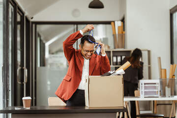 A middle-aged Asian businessman in a formal suit is working at his desk, preparing to resign after...