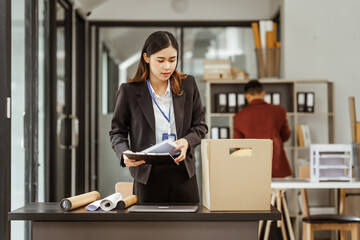 A young Asian businesswoman in a formal suit is working at her desk, preparing to resign after...