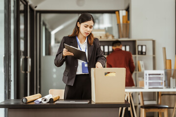 A young Asian businesswoman in a formal suit is working at her desk, preparing to resign after...