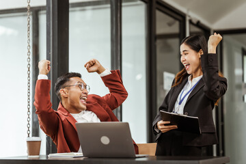 Middle-aged businessman and young Asian businesswoman work together at their desks, cooperation,...