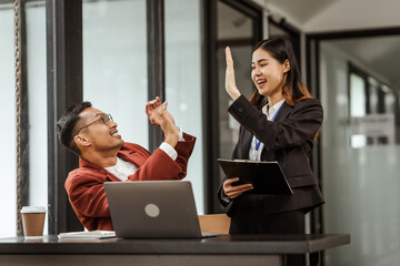 Middle-aged businessman and young Asian businesswoman work together at their desks, cooperation,...