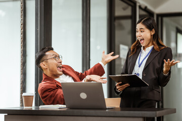 Middle-aged businessman and young Asian businesswoman work together at their desks, cooperation,...