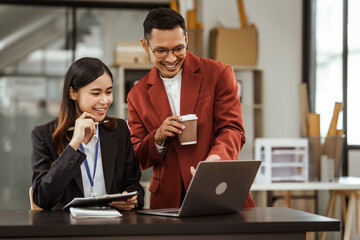 Middle-aged businessman and young Asian businesswoman diligently working at desks, managing tasks as recruitment, training, performance management, inclusive organizational culture.